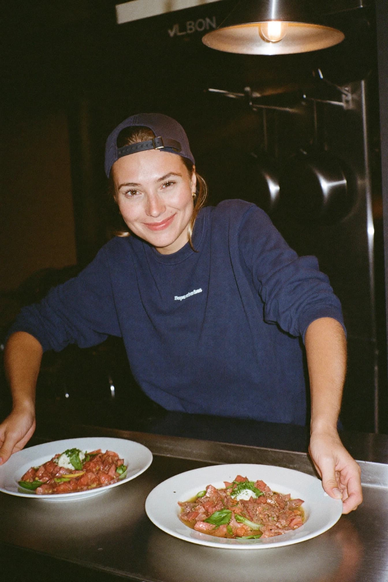 A cook at the kitchen pass sending out two plates under the heat lamp.